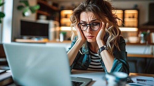 Image of frazzled female entrepreneur working remotely on computer appearing anxious fatigued and flooded.